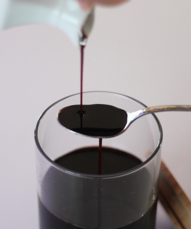 Person pouring finished elderberry syrup into glass jar