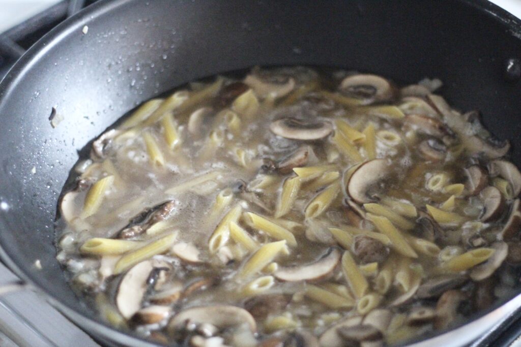 Pasta, mushrooms and onions in water on stove