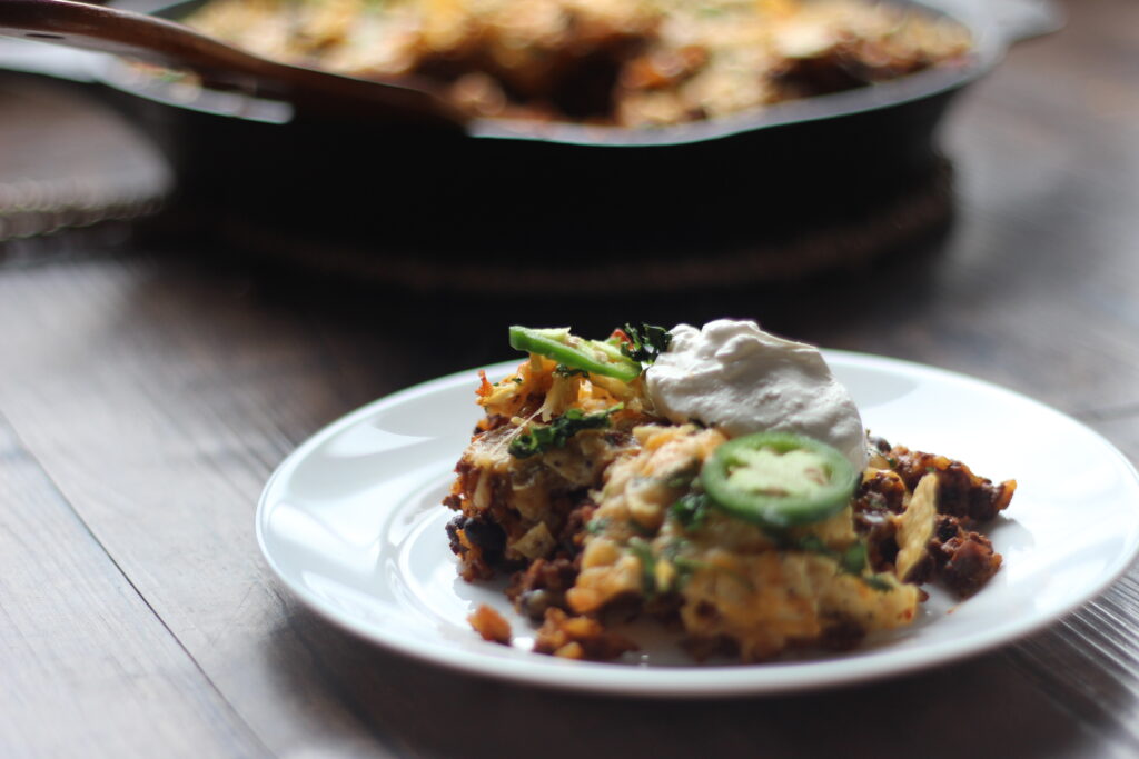 Taco skillet dinner topped with sour cream and jalapeños on white plate