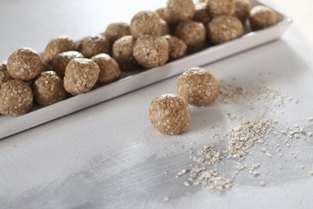 Oatmeal peanut butter balls on long white tray with oatmeal spilled on counter top